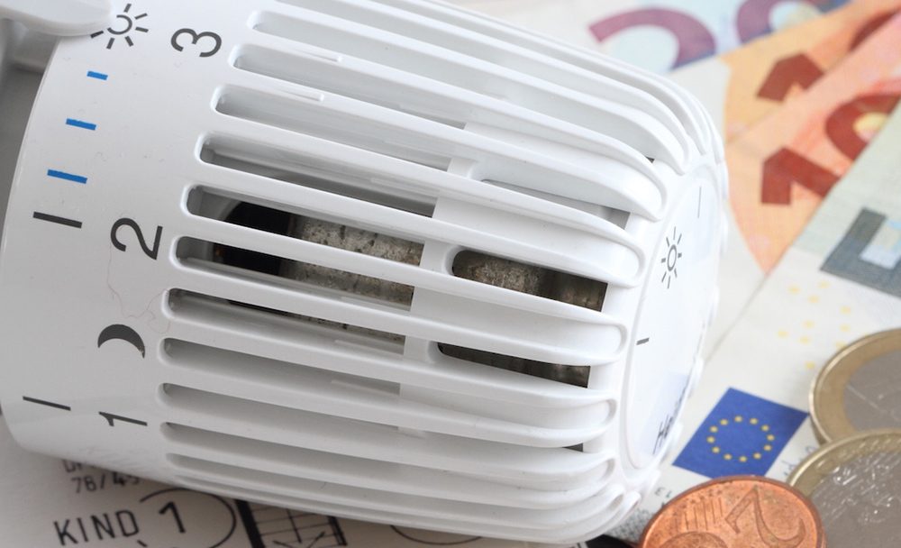 Heizungsthermostat mit Geldscheinen auf einem Bauplan